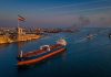 US Strikes on Iran: Self-Defense Strikes Target Missile Sites and Boats Amid Peace Talks Oil tanker sailing through the Strait of Hormuz during US strikes on Iran, with Iranian flag flying near Bandar Abbas and U.S. naval ships patrolling nearby
