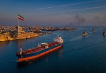 US Strikes on Iran: Self-Defense Strikes Target Missile Sites and Boats Amid Peace Talks Oil tanker sailing through the Strait of Hormuz during US strikes on Iran, with Iranian flag flying near Bandar Abbas and U.S. naval ships patrolling nearby
